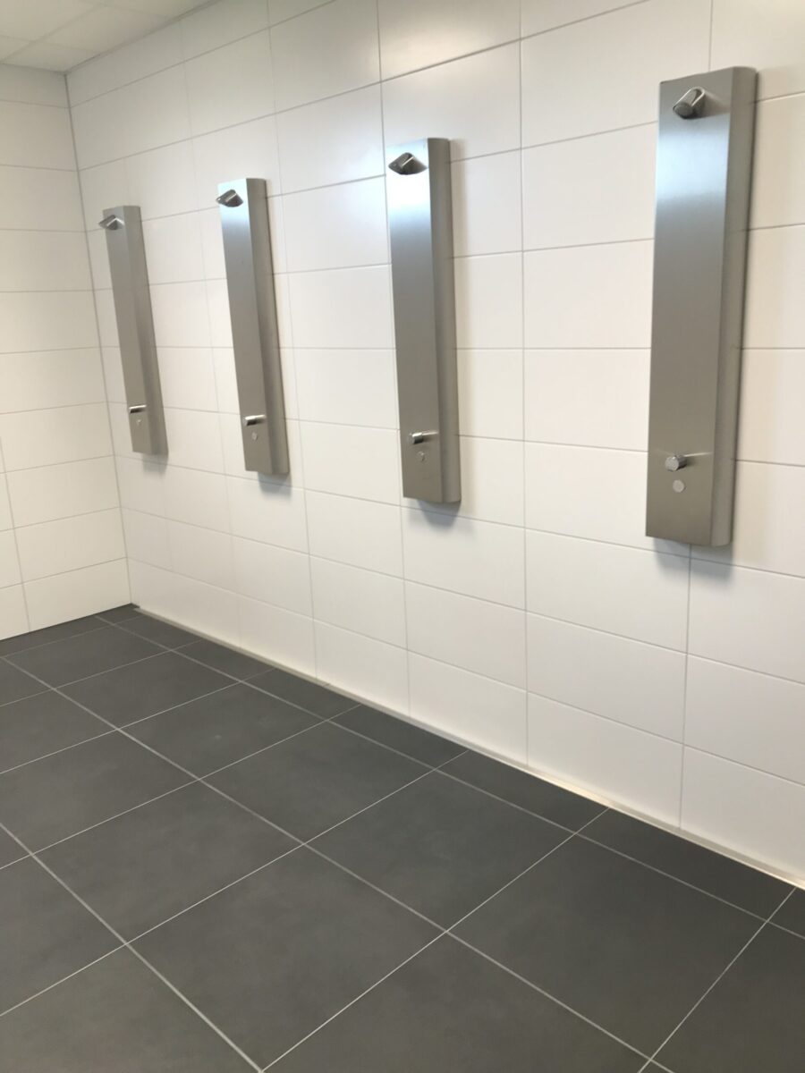"Wandbündiger Einbau einer Duschrinne in Reihenduschen für eine nahtlose Optik und effiziente Entwässerung. Die bündige Integration in die Wand ermöglicht eine barrierefreie, hygienische Lösung mit optimalem Gefälle für mehrere Duschplätze."